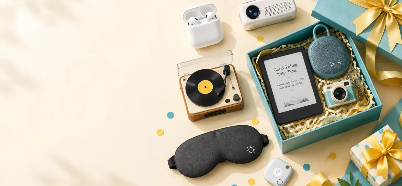 Flat-lay of gadget gift ideas including earbuds, a mini speaker, a portable projector and an e-reader beside a gift box